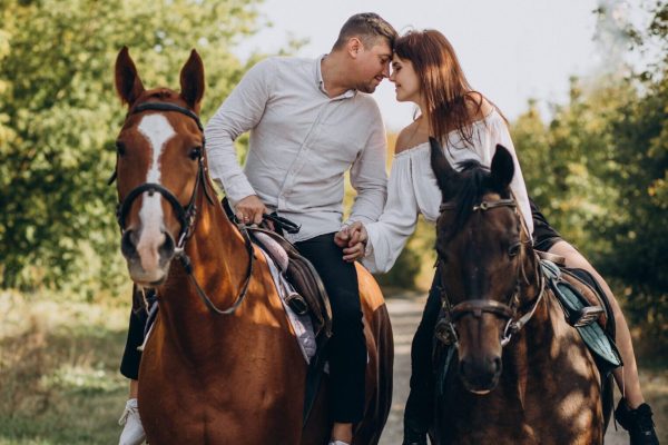 Young couple riding horses together in park