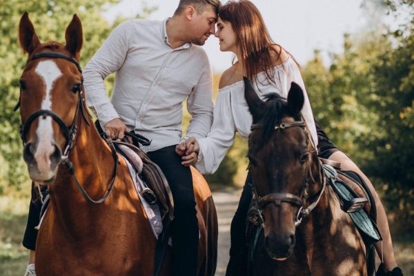 Young couple riding horses together in park